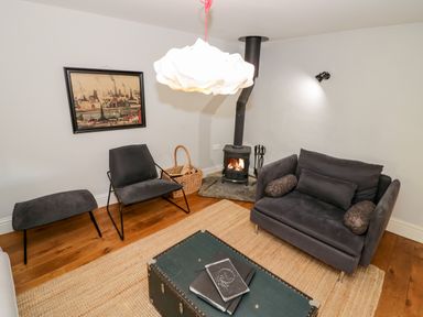 A small living room with a black chair and ottoman a two-seater sofa a wood-burning stove and a trunk used as a coffee table at The Old Stables in Chipping Campden