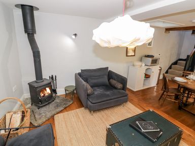 A living room with a wood burning stove armchairs a rug a chest and a dining table at The Old Stables in Chipping Campden