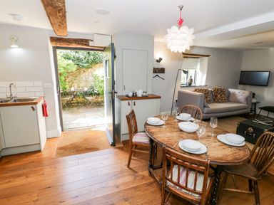 A dining area with a wooden table set for four and a living room with a sofa and TV at The Old Stables in Chipping Campden