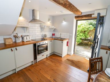 A kitchen with wooden countertops an oven toaster and sink opening to an outdoor patio with table and chairs at The Old Stables in Chipping Campden