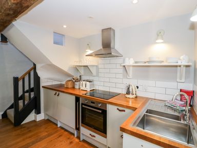 A kitchen with wooden countertops a stove an oven a toaster a kettle a sink stairs in the corner at The Old Stables in Chipping Campden