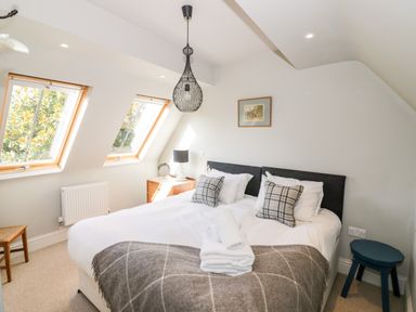 A bedroom with a double bed pillows and folded towels near two angled windows at The Old Stables in Chipping Campden