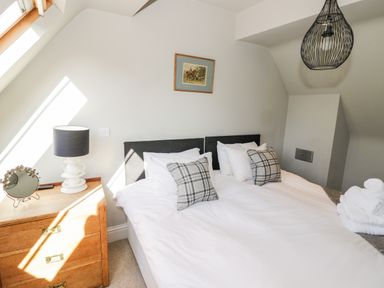 A bedroom with a bed with pillows and a wooden chest of drawers with a lamp at The Old Stables in Chipping Campden