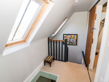 A stairway landing with skylights a small bench a framed painting and a sliding wooden door at The Old Stables in Chipping Campden