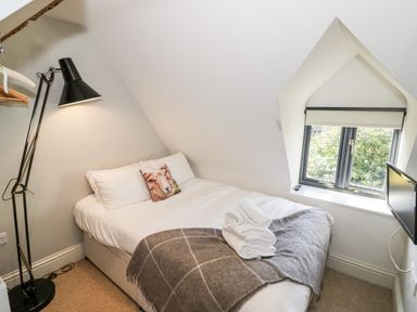 A bedroom with a double bed a floor lamp a window and a small wall-mounted television at The Old Stables in Chipping Campden