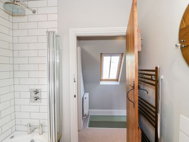 A bathroom with a shower, bathtub, towel rack, open door and a window at The Old Stables in Chipping Campden