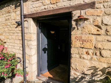 A stone building entrance with a dark door and a sign reading The Old Stables with a lantern above at The Old Stables in Chipping Campden