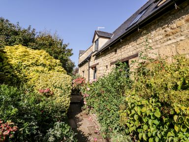 A garden pathway with various bushes and flowering plants beside a stone building at The Old Stables in Chipping Campden