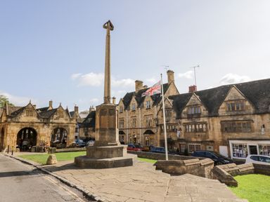 A stone monument and a flagpole with a union jack flag in front of historic stone buildings in a town square