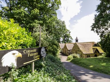 A pathway leading to stone buildings with a sign for Cotswold Falconry Centre surrounded by greenery at The Old Stables in Chipping Campden