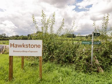A sign for Hawkstone Brewery Shop Taproom next to green public footpath signs in a rural area