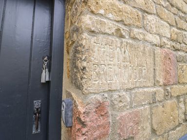 A stone wall with the words The Old Brewhouse carved into it next to a black door with keys in the lock at The Old Brewhouse in Chipping Campden
