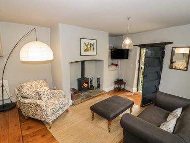 A living room with a wood stove fireplace a patterned armchair a dark sofa a large ottoman and an arched floor lamp at The Old Brewhouse in Chipping Campden
