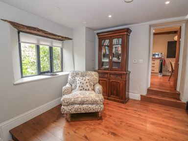 A sitting area with a patterned armchair and a wooden bookcase near a window at The Old Brewhouse in Chipping Campden