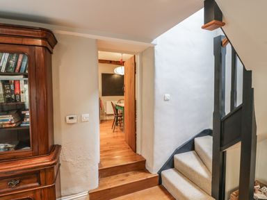 A hallway with a wooden bookcase stairs with carpet and a door leading to a dining room at The Old Brewhouse in Chipping Campden