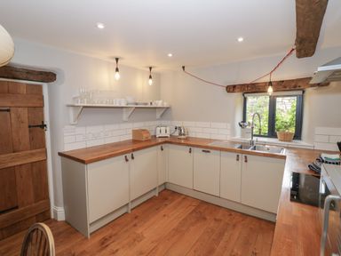A kitchen with wooden countertops cabinets a sink window and hanging light bulbs at The Old Brewhouse in Chipping Campden