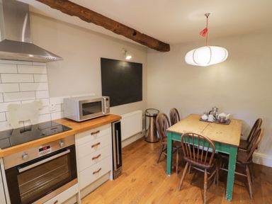 A kitchen with wooden floor a table and chairs a microwave an oven and a blackboard at The Old Brewhouse in Chipping Campden