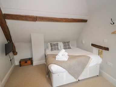 A bedroom with a double bed folded blankets and pillows exposed wooden beams a wall-mounted tv and a small window at The Old Brewhouse in Chipping Campden