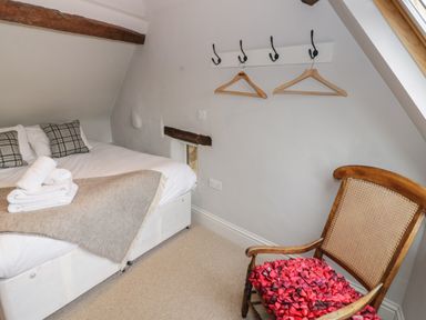 A bedroom with a bed with folded towels and pillows and a wooden chair with a cushion at The Old Brewhouse in Chipping Campden
