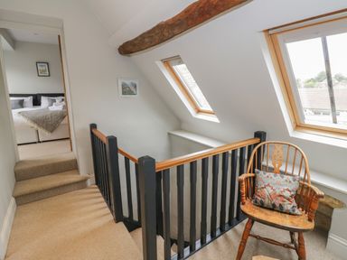 A stair landing with wooden chair and pillow near windows and a view into a bedroom at The Old Brewhouse in Chipping Campden