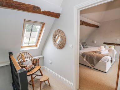 A hallway with a wooden chair and footstool and a round wall mirror next to a bedroom with a bed and folded towels at The Old Brewhouse in Chipping Campden