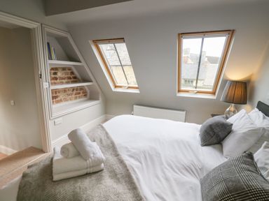 A bedroom with a double bed with folded towels a lamp bedside windows and built in shelves at The Old Brewhouse in Chipping Campden