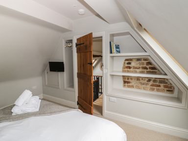 A bedroom corner with a wooden door open shelves with books and exposed brick at The Old Brewhouse in Chipping Campden