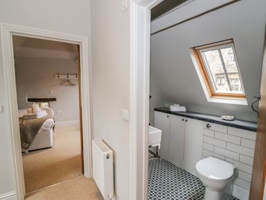 A hallway showing a doorway to a bedroom with a bed and towels and a bathroom with a toilet and skylight at The Old Brewhouse in Chipping Campden