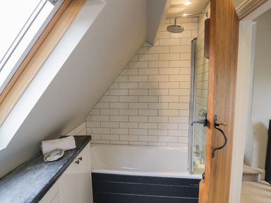A bathroom with a bathtub shower and tiled wall under a slanted ceiling at The Old Brewhouse in Chipping Campden