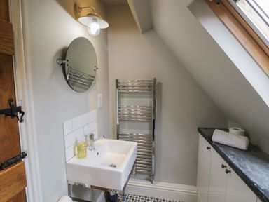 A small bathroom with a wall-mounted sink mirror towel rack and cabinet under a skylight at The Old Brewhouse in Chipping Campden