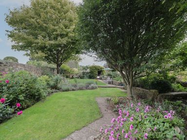 A garden with trees flowers stone walls and outdoor seating at The Old Brewhouse in Chipping Campden