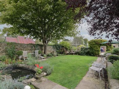 A garden with a stone wall wooden chairs a pond and a grassy lawn at The Old Brewhouse in Chipping Campden