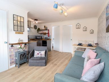 A living room with a sofa and armchair next to a small stove and a dining table with two place settings at 72 in Hemsby