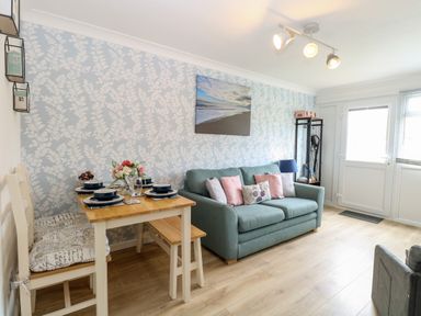 A living room with a dining table set for four and a sofa with cushions at 72 in Hemsby