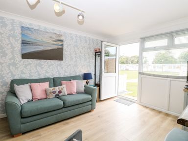 A living room with a green sofa and cushions next to an open door and large window at 72 in Hemsby