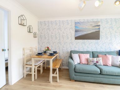 A dining table set with plates and glasses beside a blue sofa with cushions and wall art in a living room at 72 in Hemsby