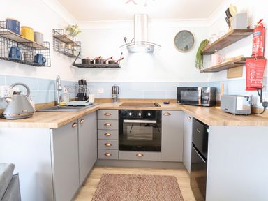 A kitchen with wooden countertops gray cabinets stove oven microwave kettle and open shelves at 72 in Hemsby