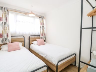 A bedroom with two single beds white bedding and pink cushions at 72 in Hemsby