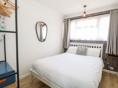 A bedroom with a white bed and a decorative cushion under a window with curtains at 72 in Hemsby