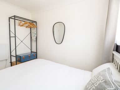 A bedroom with a white bed a grey pillow a wall mirror and a clothing rack with hangers and an ironing board at 72 in Hemsby