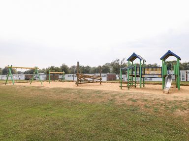 A playground with swings, wooden climbing structures, and a slide on sand near mobile homes at 72 in Hemsby