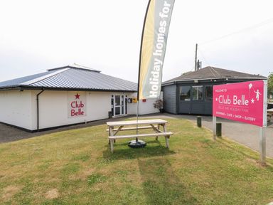 An outdoor area with a picnic table a flag and two buildings with Club Belle signs at Belle Aire Holiday Park