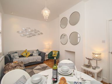 A living room with a sofa, green armchair, round mirrors, dining table with dishes and wine bottle at The Cottage in Weymouth