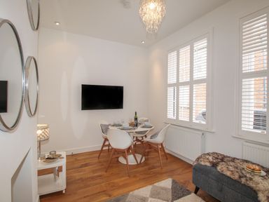 A dining area with a round table set for four people and white chairs next to windows with shutters at The Cottage in Weymouth