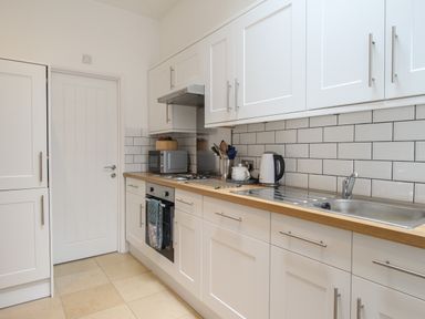 A kitchen with white cabinets a wooden countertop a sink a kettle a microwave and an oven at The Cottage in Weymouth