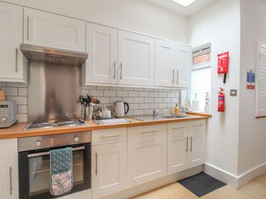 A kitchen with white cabinets a stove a microwave and a sink at The Cottage in Weymouth