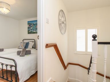 A bedroom with two beds and folded towels next to a staircase with a wooden handrail and a clock on the wall at The Cottage in Weymouth
