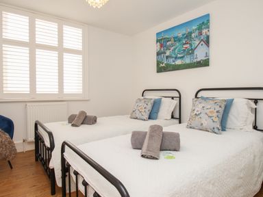 A bedroom with two single beds with floral cushions and rolled towels on each bed at The Cottage in Weymouth