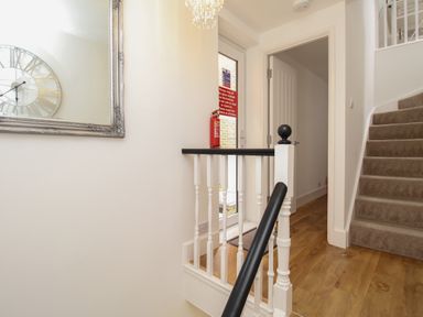 A staircase with carpeted steps a wooden floor a large wall mirror and a fire extinguisher near a glass door at The Cottage in Weymouth