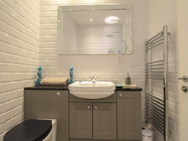 A bathroom with a sink, mirror, toilet, towel rack, and decorative items at The Cottage in Weymouth